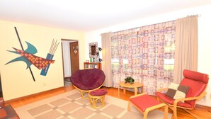 A living room with a large window, a red chair, a purple chair, a small table, and a wall decoration. - Castle View - A Rancher With a View! (Berkeley Springs)