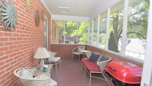 A covered patio with wicker furniture, a grill, and a view of trees and houses. - Castle View - A Rancher With a View! (Berkeley Springs)