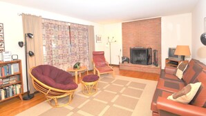 A living room with a fireplace, a bookshelf, a red leather sofa, and a wicker chair. - Castle View - A Rancher With a View! (Berkeley Springs)