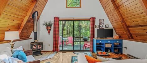 Um quarto de sótão aconchegante, com teto de madeira, lareira, televisão e uma grande janela com vista para uma floresta.