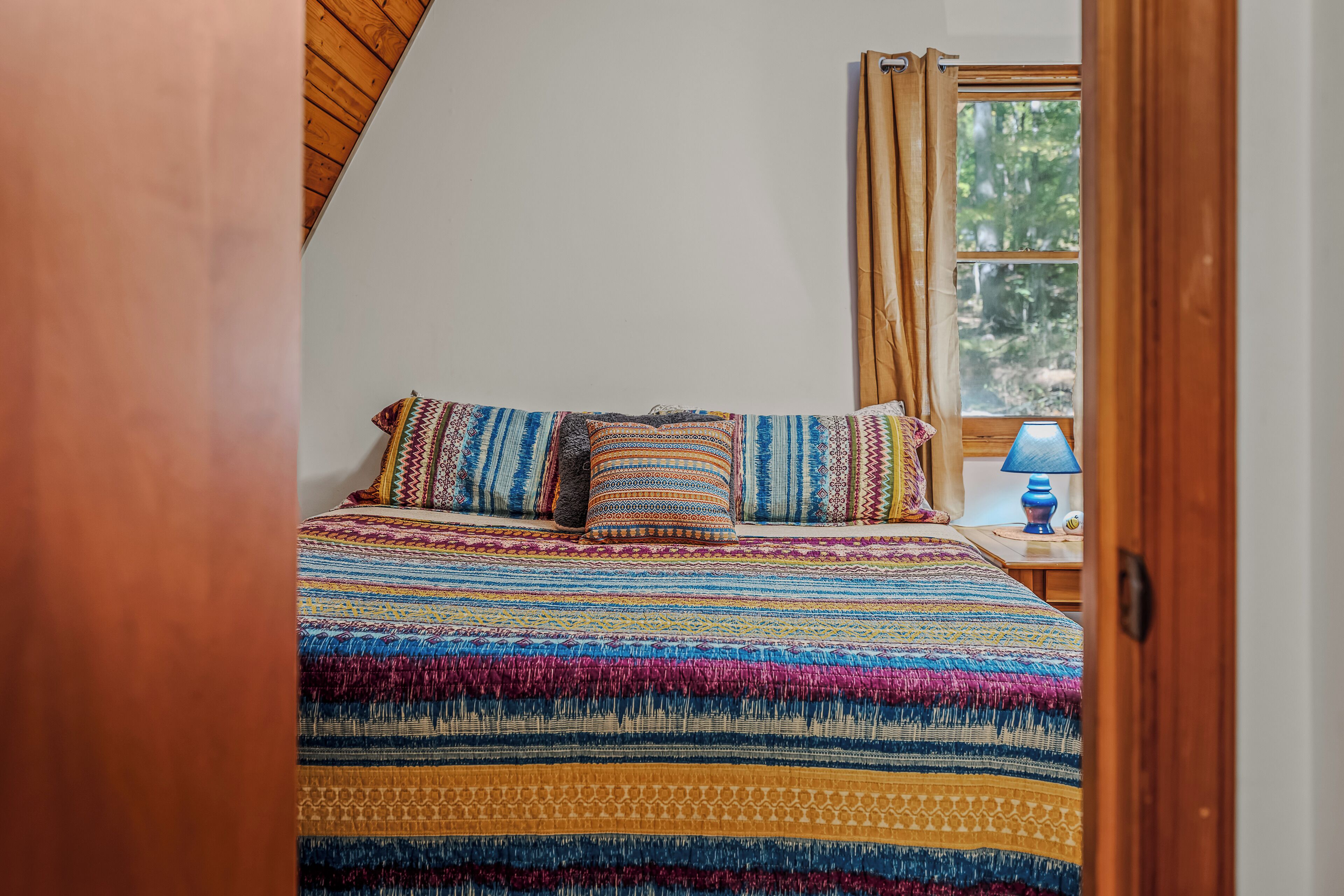 A bed with a colorful, striped bedspread and multiple pillows.