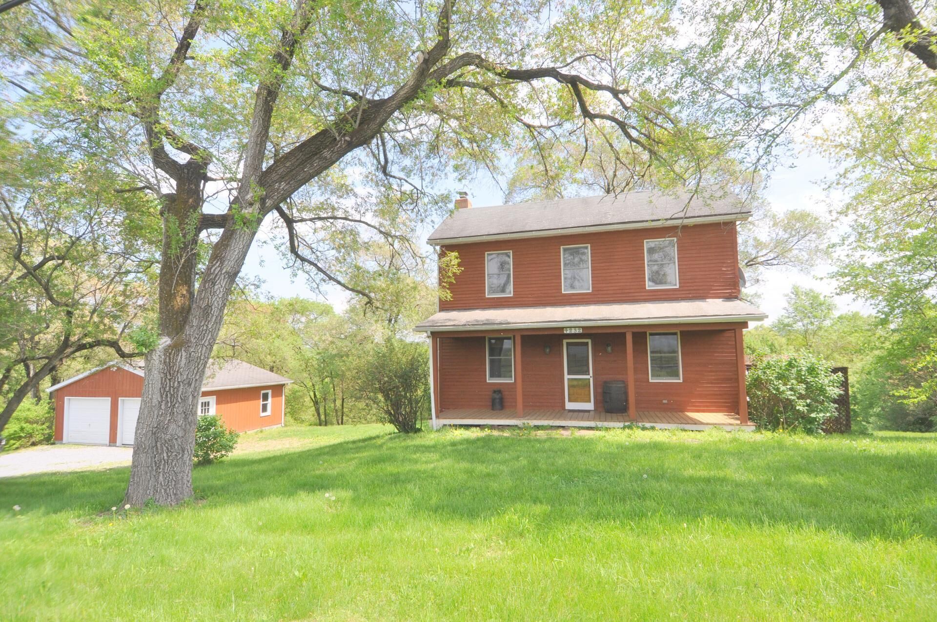 A two-story red house with a front porch, surrounded by a well-maintained lawn and trees.