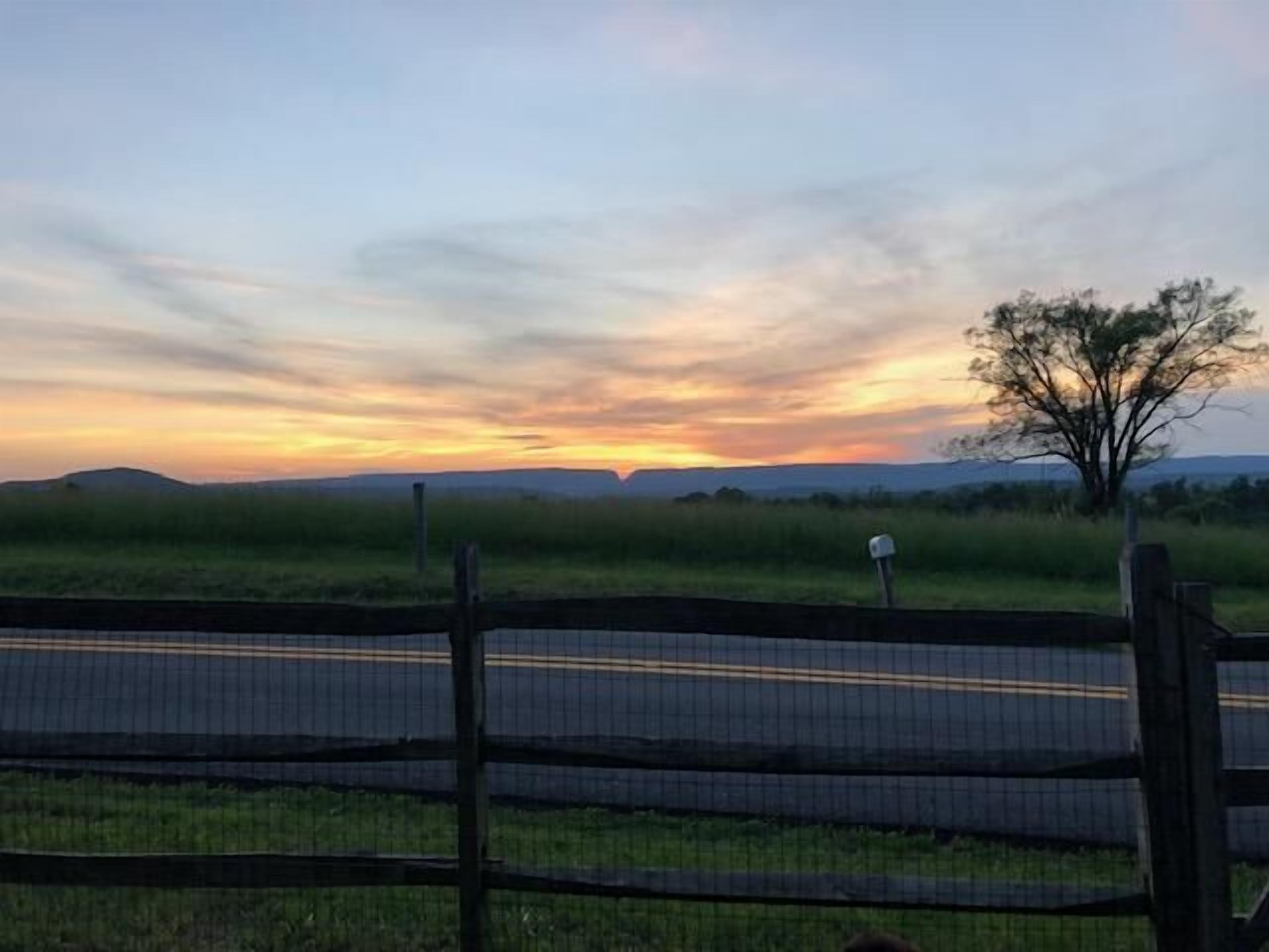 A sunset over a grassy landscape with a fence in the foreground.