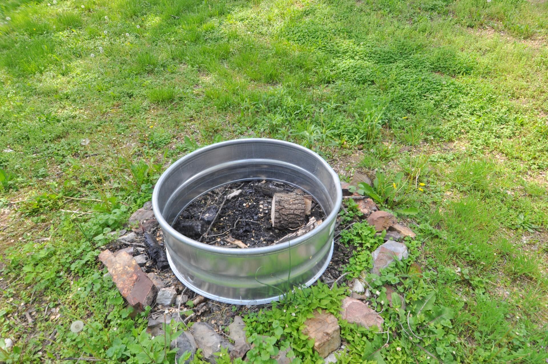 Un hogar de metal con madera quemada y ceniza, rodeado de rocas y vegetación.