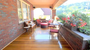 A covered patio with brick walls, wooden flooring, and outdoor seating including a bench, chairs, and a table. - Aunt Beas Bungalow - Right in Town! (Berkeley Springs)