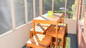 A covered patio with a wooden table and chairs, large windows, and a green patterned rug. - Aunt Beas Bungalow - Right in Town! (Berkeley Springs)