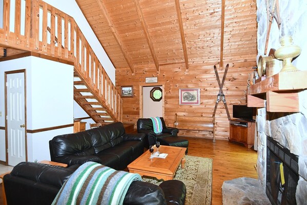 A wooden interior with a staircase, leather sofas, a fireplace, and a television.