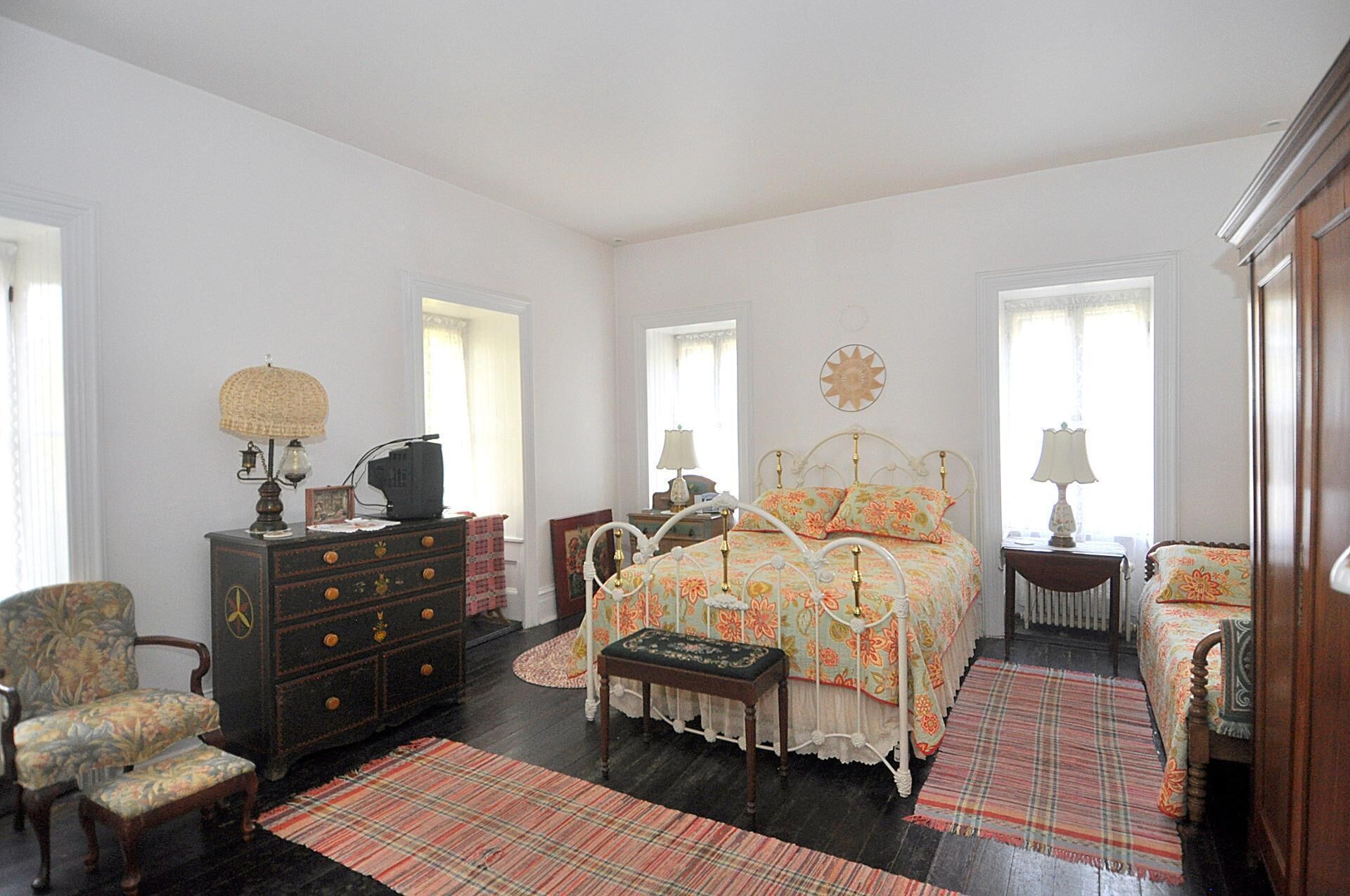 A bedroom with a bed, dresser, chair, and a large window.