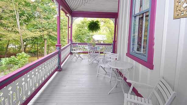 A covered porch with white and pink railings, white chairs, and a table. - Manor at Berkeley Springs (Berkeley Springs)