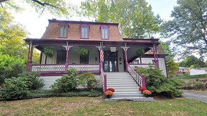 A two-story house with a porch, a staircase, and a sign indicating the breakfast area is open. - Manor at Berkeley Springs (Berkeley Springs)