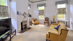 A living room with a fireplace, two armchairs, a sofa, a television, and a lamp. - Manor at Berkeley Springs (Berkeley Springs)