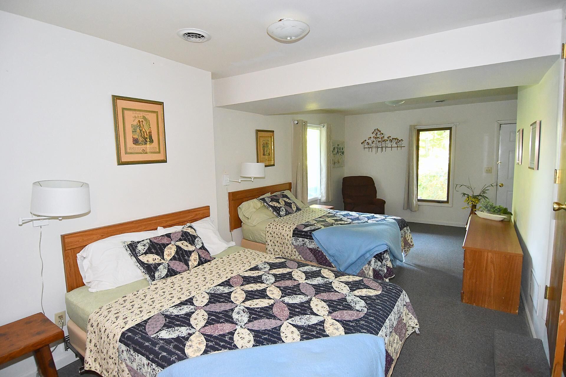A room with two beds, a chair, a desk, and a window.