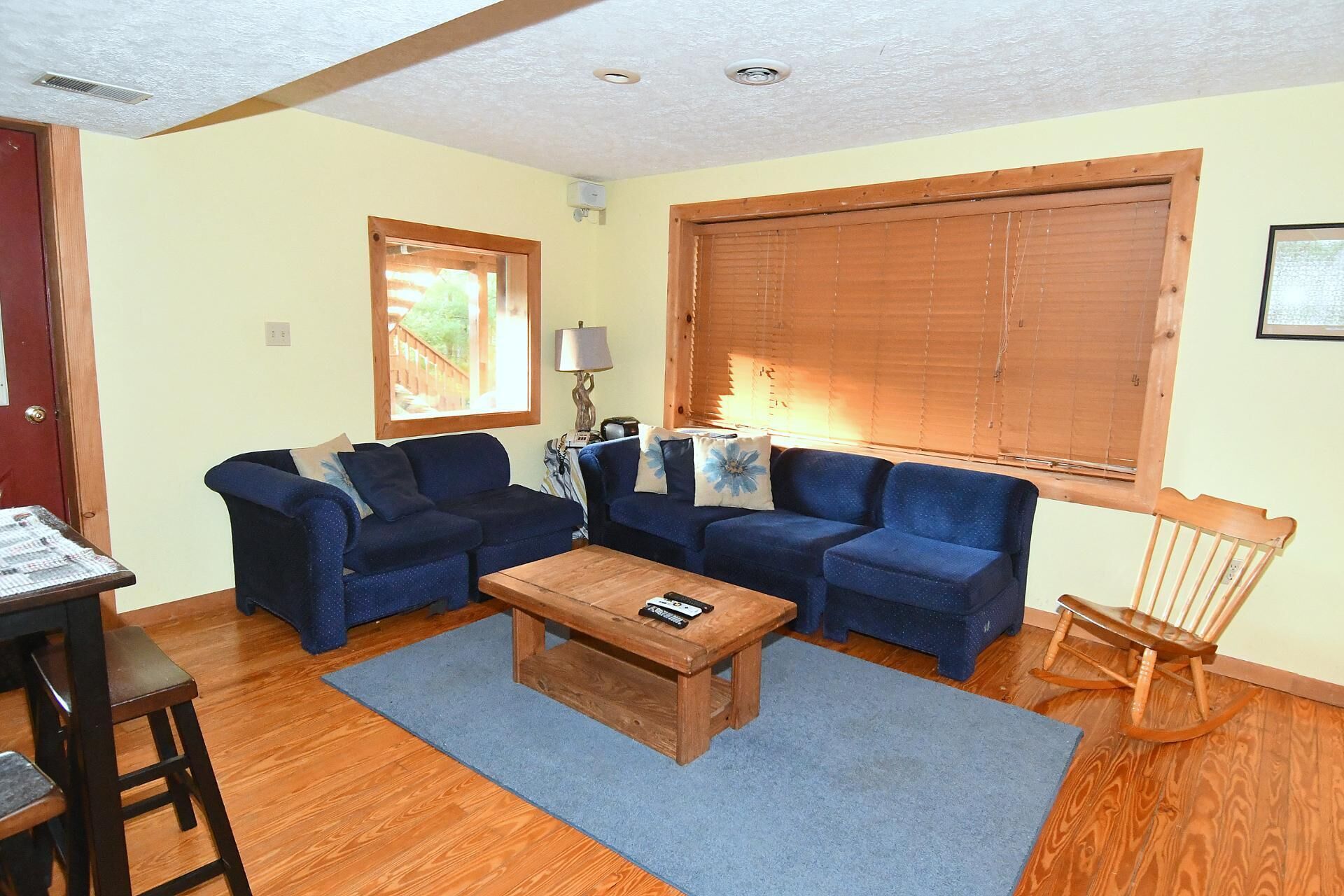 A living room with two blue sofas, a wooden coffee table, a rocking chair, and a window with blinds.