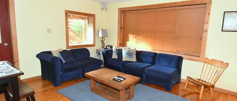 A living room with two blue sofas, a wooden coffee table, a rocking chair, and a window with blinds.