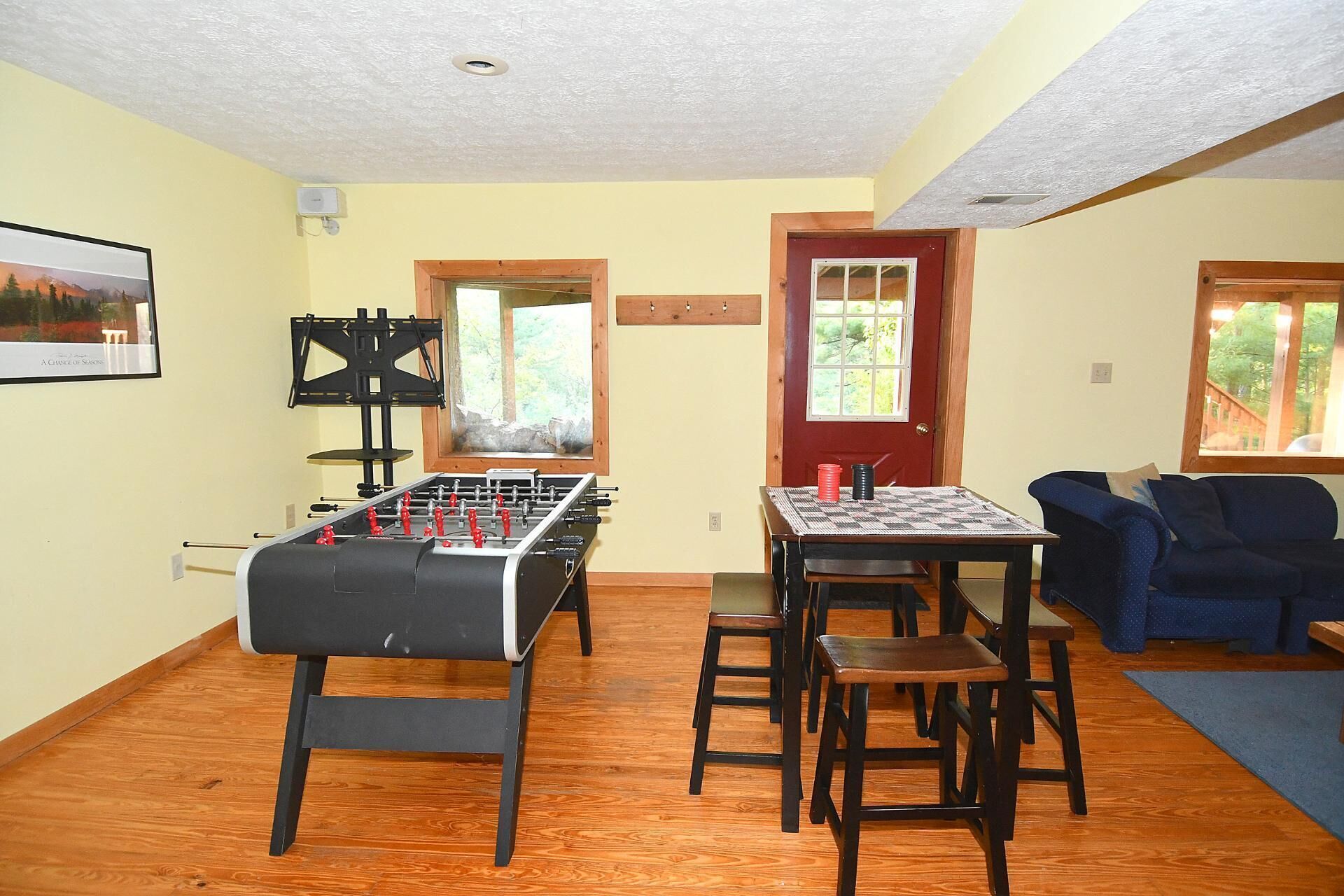 A cozy room with a foosball table, a window with a view of greenery, and a blue couch.