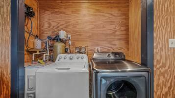 A compact laundry room with a washing machine and a dryer, wooden walls, and visible plumbing.