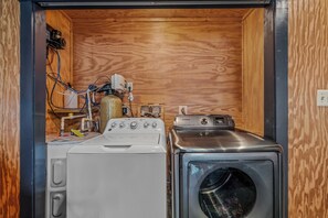 A compact laundry room with a washing machine and a dryer, wooden walls, and visible plumbing. - Whispering Hills - Couples Getaway (Berkeley Springs)