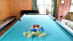 A pool table with a triangular arrangement of billiard balls, two empty glasses, and a hanging decorative item. - Whispering Hills - Couples Getaway (Berkeley Springs)
