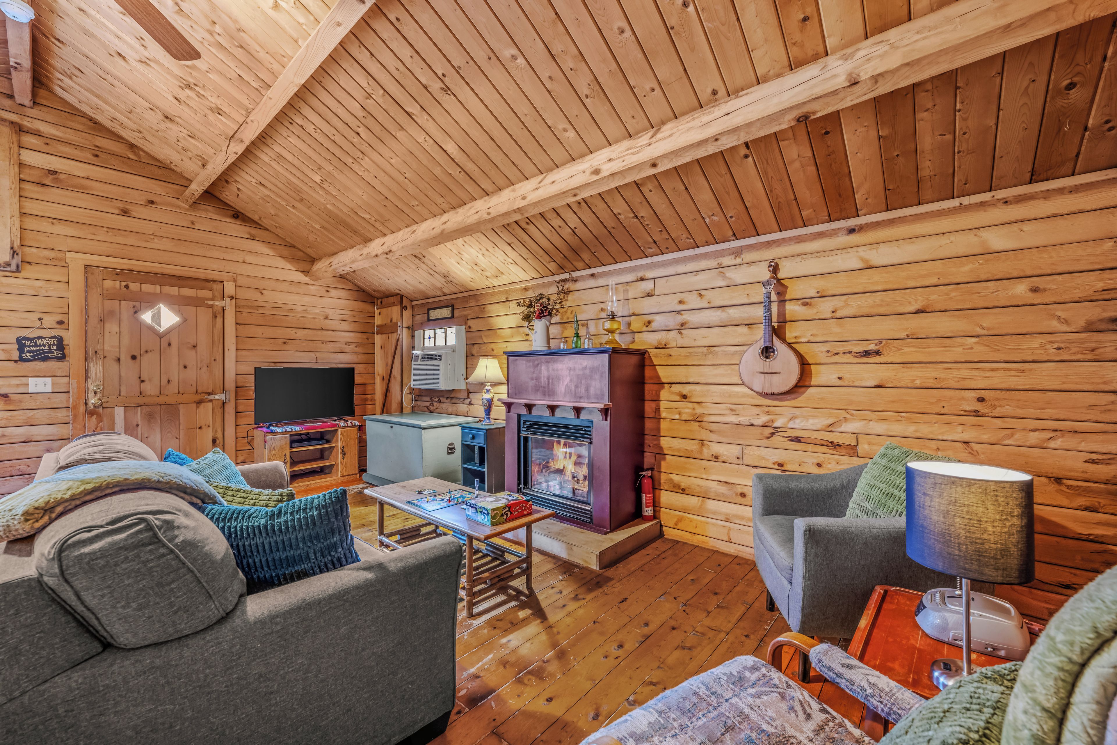 A cozy cabin interior with a fireplace, wooden walls, a sofa, and a table with board games.