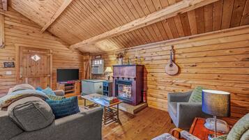 A cozy cabin interior with a fireplace, wooden walls, a sofa, and a table with board games.