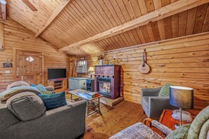 Interior acogedor de una cabaña con chimenea, paredes de madera, un sofá y una mesa con juegos de mesa.