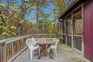 A wooden deck with a table and chairs, surrounded by trees with autumn foliage. - Whispering Hills - Couples Getaway (Berkeley Springs)