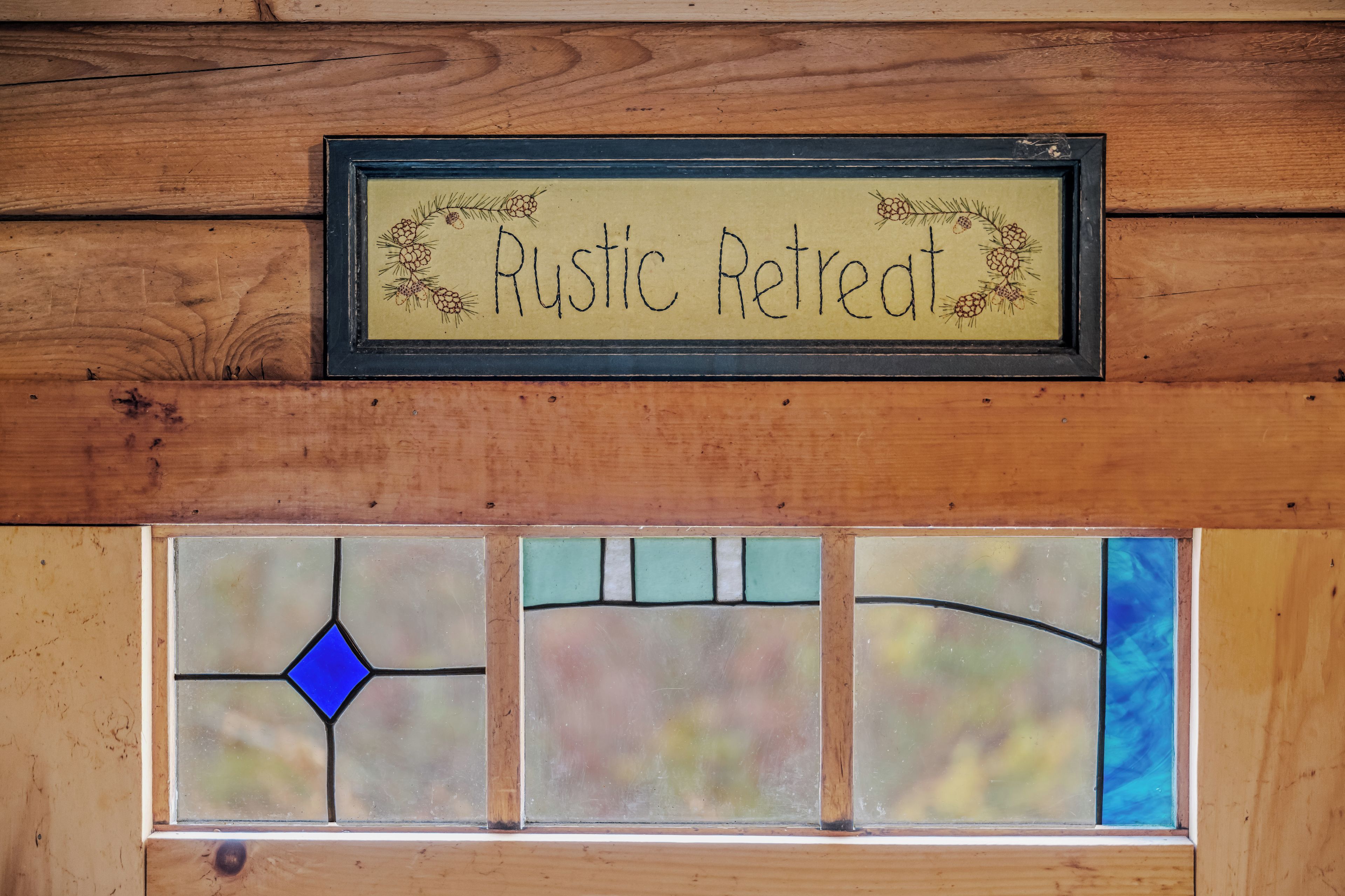 Un mur en bois sur lequel est fixée une plaque encadrée portant l’inscription « Refuge rustique ». En dessous de la plaque, on trouve un vitrail aux motifs géométriques et à la forme de losange bleue.