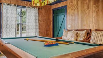 A pool table with balls and cues, a window with curtains, and a wooden wall.