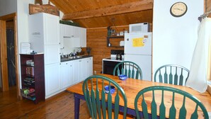 A cozy kitchen with wooden cabinets, a dining table with chairs, and a clock on the wall. - Whispering Hills - Couples Getaway (Berkeley Springs)