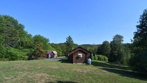 A rustic cabin with a small porch and a large water tank in a grassy field surrounded by trees. - Whispering Hills - Couples Getaway (Berkeley Springs)