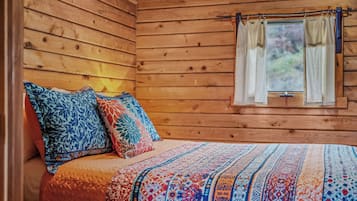Dormitorio de cabaña de madera con cama, almohadas y ventana con cortinas.