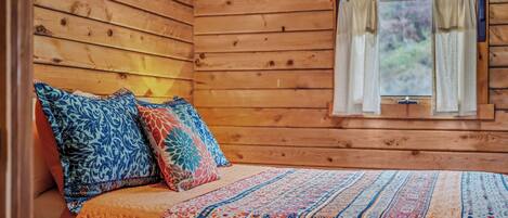 A wooden cabin bedroom with a bed, pillows, and a window with curtains.