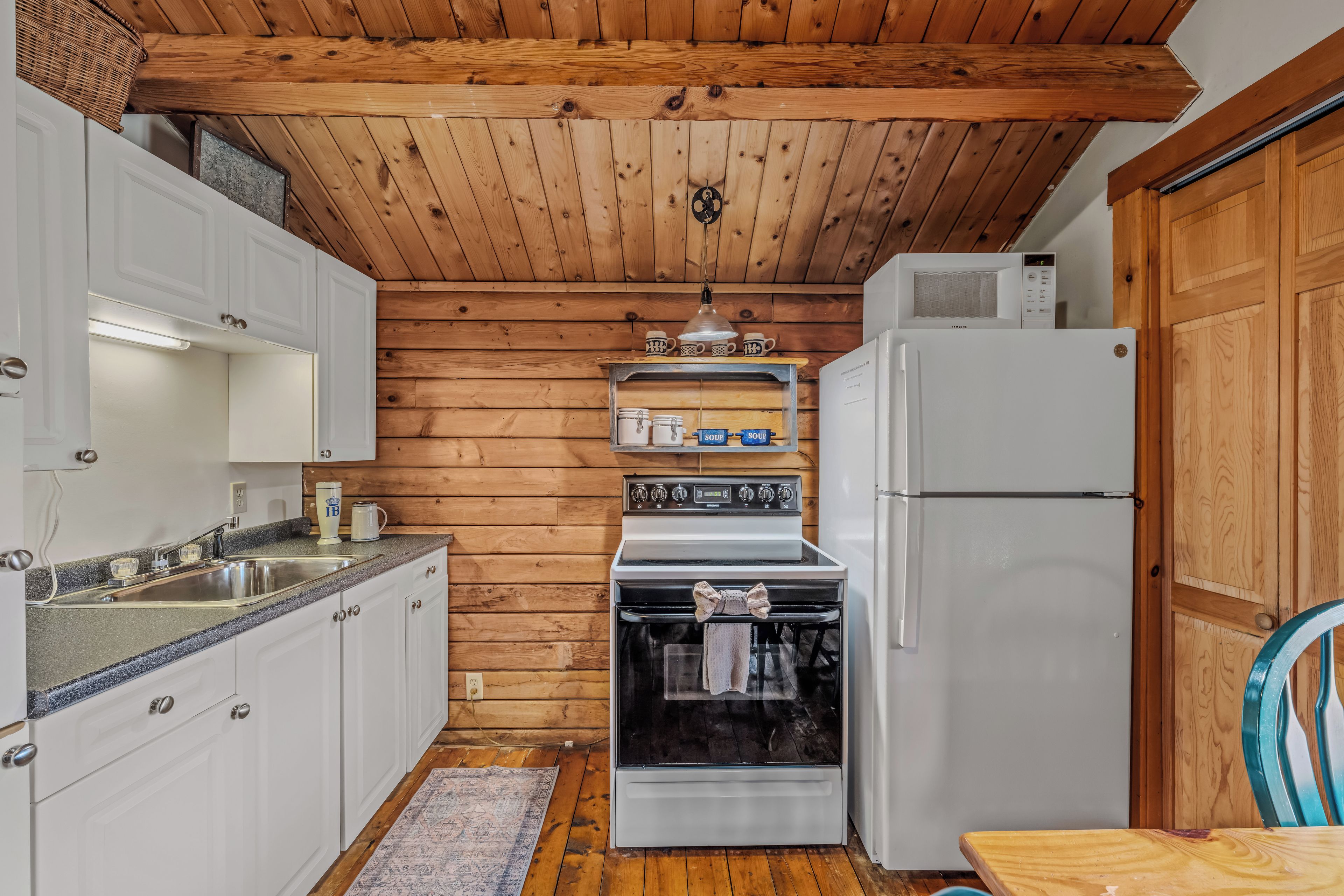 A compact kitchen with wooden panel walls, white cabinetry, a stainless steel sink, a stove, and a refrigerator.