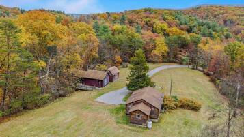 A rural property with two wooden cabins and a barn, surrounded by a forested area with autumn foliage.