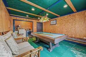 Una mesa de billar en una habitación con paredes y techo de madera, un sofá y una lavadora.