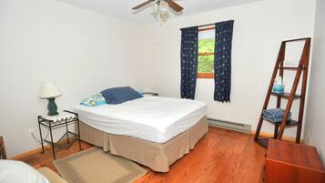 A bedroom with a bed, a nightstand, a lamp, a window with curtains, a ceiling fan, and a wooden ladder.