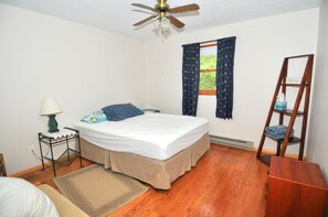 Une chambre à coucher comprenant un lit, une table de chevet, une lampe, une fenêtre avec des rideaux, un ventilateur de plafond et une échelle en bois.