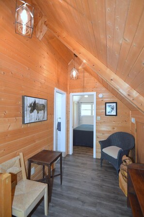 Une charmante cabane en bois avec une chambre à coucher située en mezzanine, un coin repas et un espace salon.