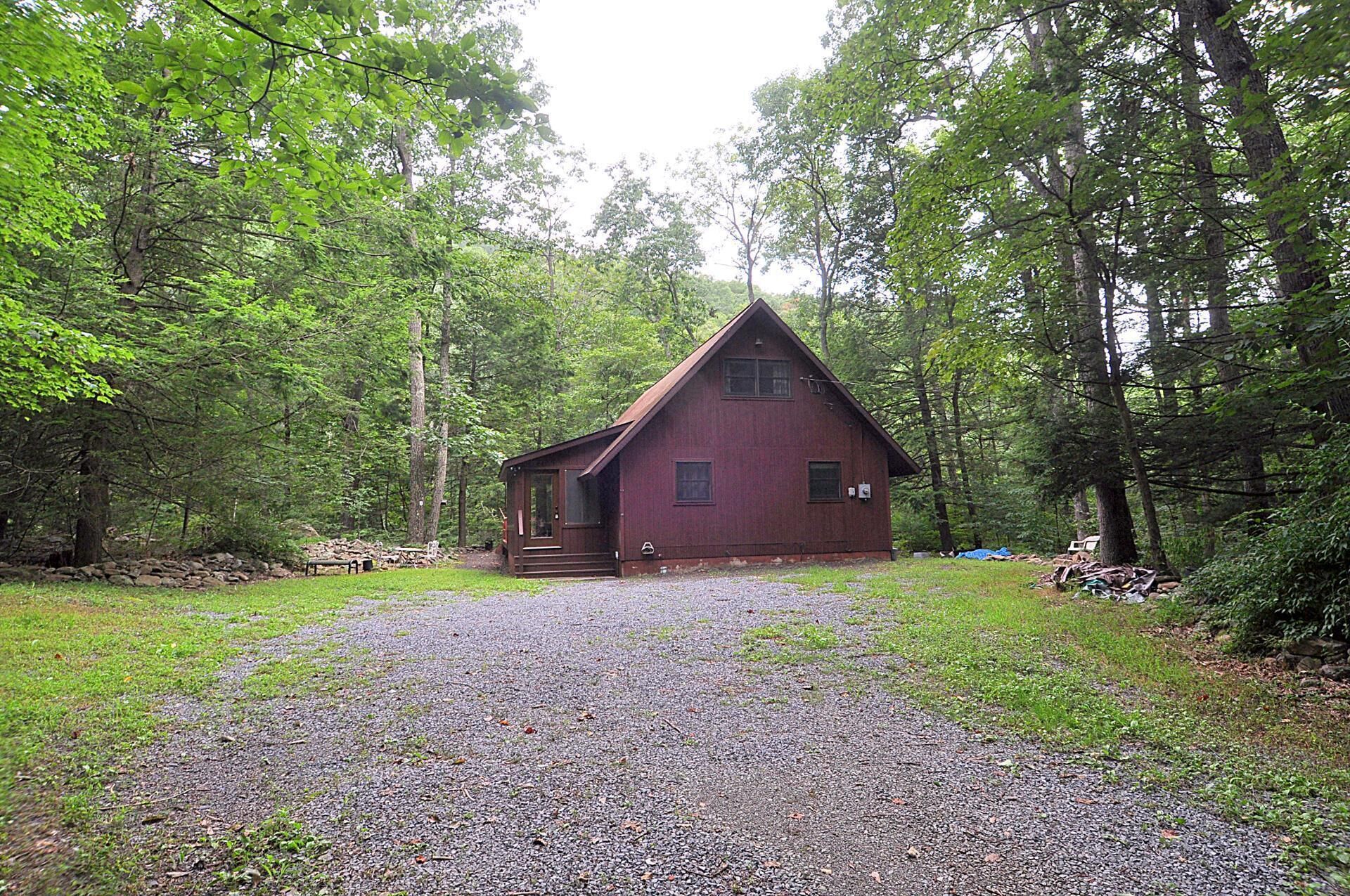 A rustic cabin with a gravel driveway, surrounded by dense forest.