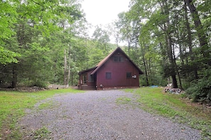 Un chalet rustique avec une allée en gravier, entouré d’une forêt dense.