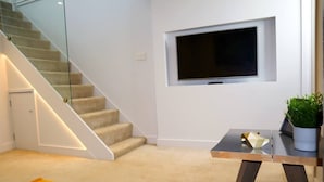 En modern inredning med en trappa, en platt-TV som är monterad på väggen, ett litet bord med en växt och en gul matta.