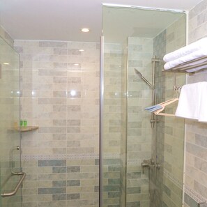 A glass-enclosed shower with a handheld showerhead and a towel rack with towels.