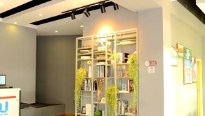 A reception area with a check-in counter, a bookshelf with books and plants, and a wall with framed artwork.