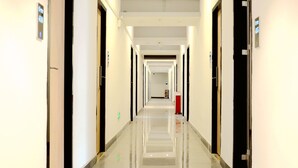 A long, well-lit hotel corridor with doors on both sides leading to rooms.
