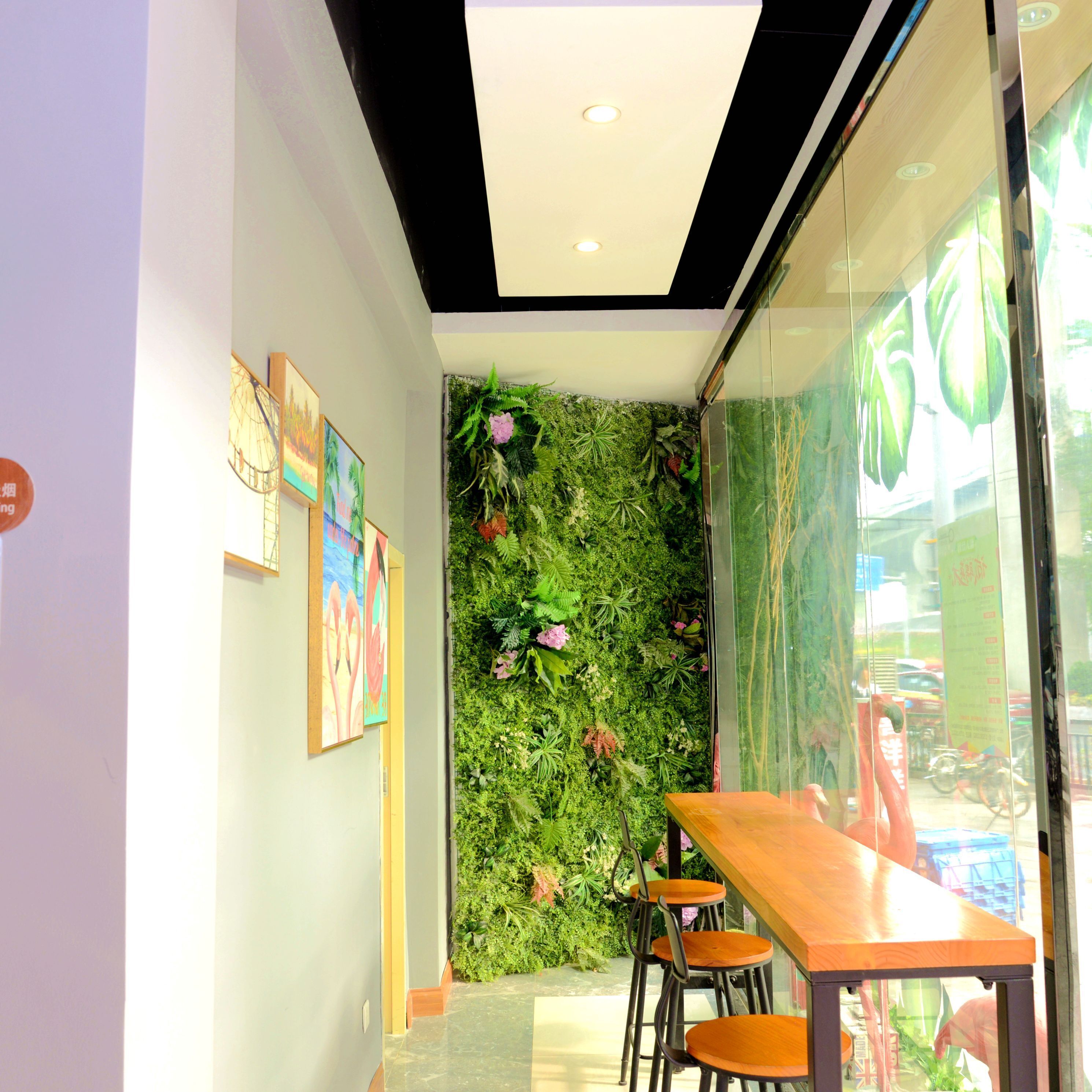 A narrow hallway with a green wall covered in plants, a wooden table with chairs, and framed artwork on the wall.