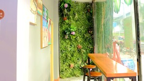 A narrow hallway with a green wall covered in plants, a wooden table with chairs, and framed artwork on the wall.