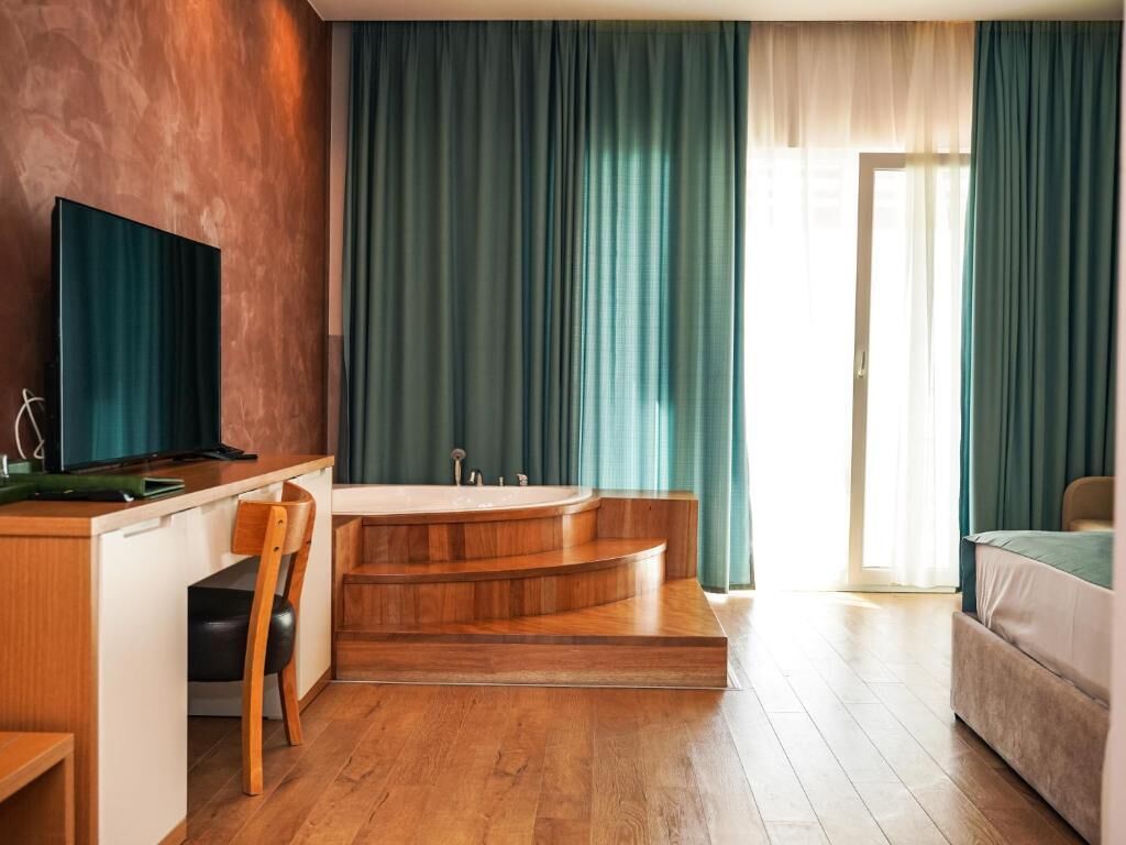 A modern hotel room with a wooden desk, a television, a bathtub, and a sofa.