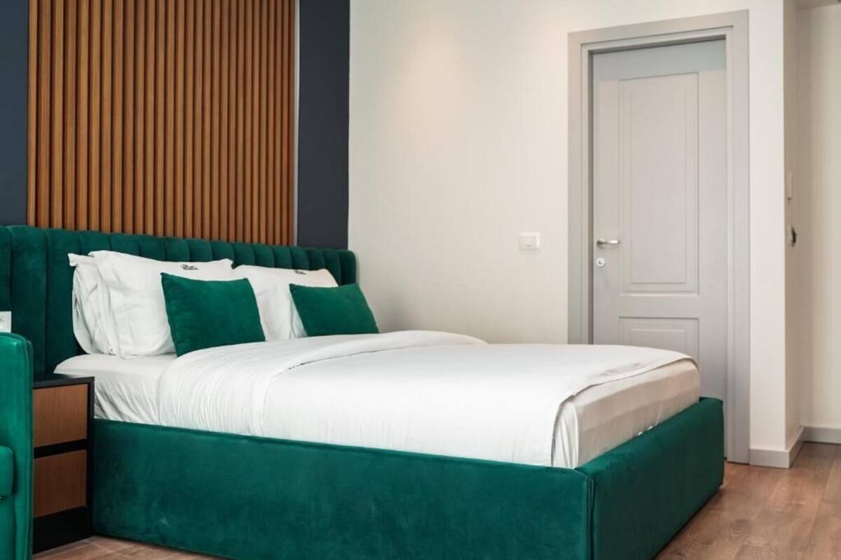 A bed with a green upholstered headboard, white bedding, and a wooden floor.