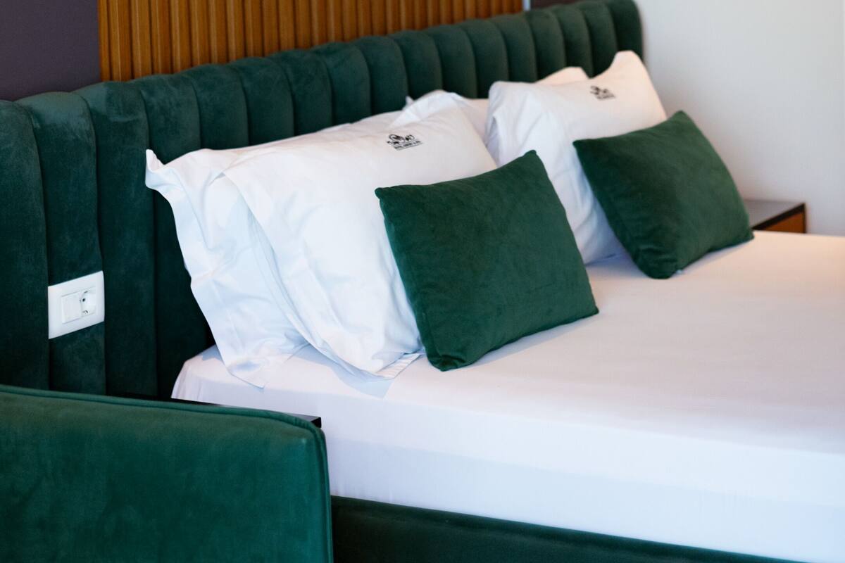 A modern hotel room with a green upholstered headboard, white bedding, and green pillows.