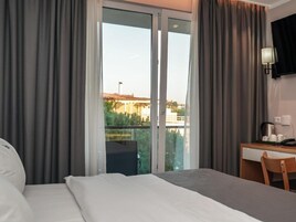 Una habitación de hotel con cama, escritorio, silla y un ventanal con cortinas.